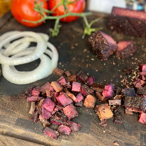 Anna Meru Alpine Smoked Vegan Cubes scattered on a dark wooden board with fresh onion rings, perfect as a plant-based bacon alternative.