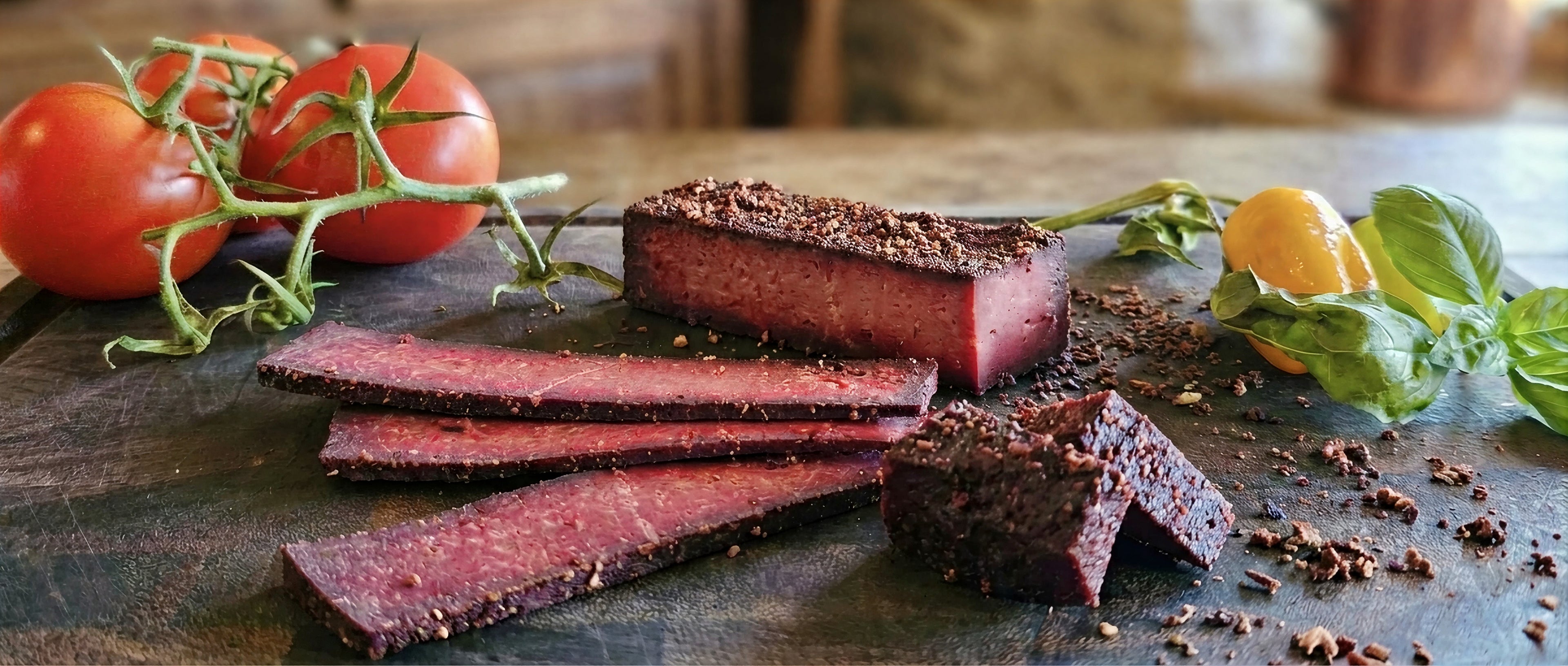 Anna Meru Schwarzgeräucherter smoked vegan cold cuts sliced on a dark wooden board with fresh vine tomatoes and herbs.
