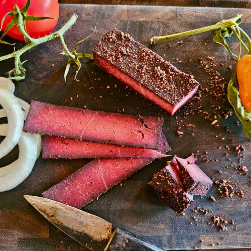Top-down view of sliced Alpine Smoked Vegan Block next to fresh white onion rings, tomatoes, and a vintage rustic knife.